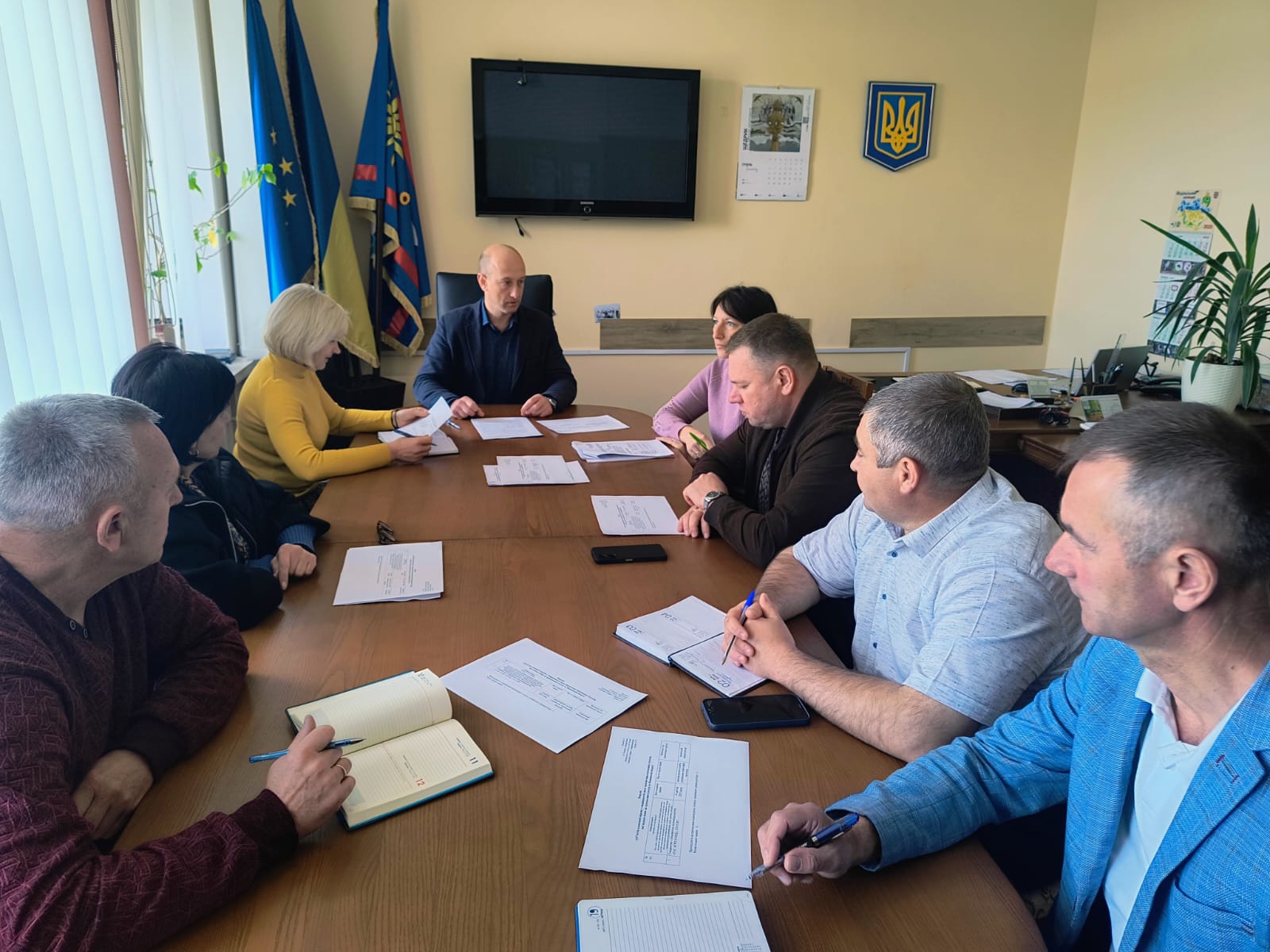 Члени комісії сидять за  робочим столом в кабінеті директора Департаменту, перед ними лежать документи