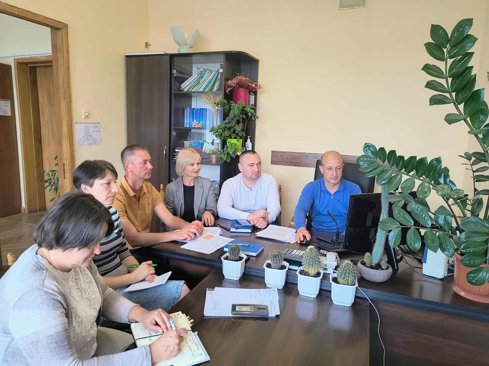 Учасники  наради сидять за робочим столом у кабінеті, перед ними монітор комп'ютера