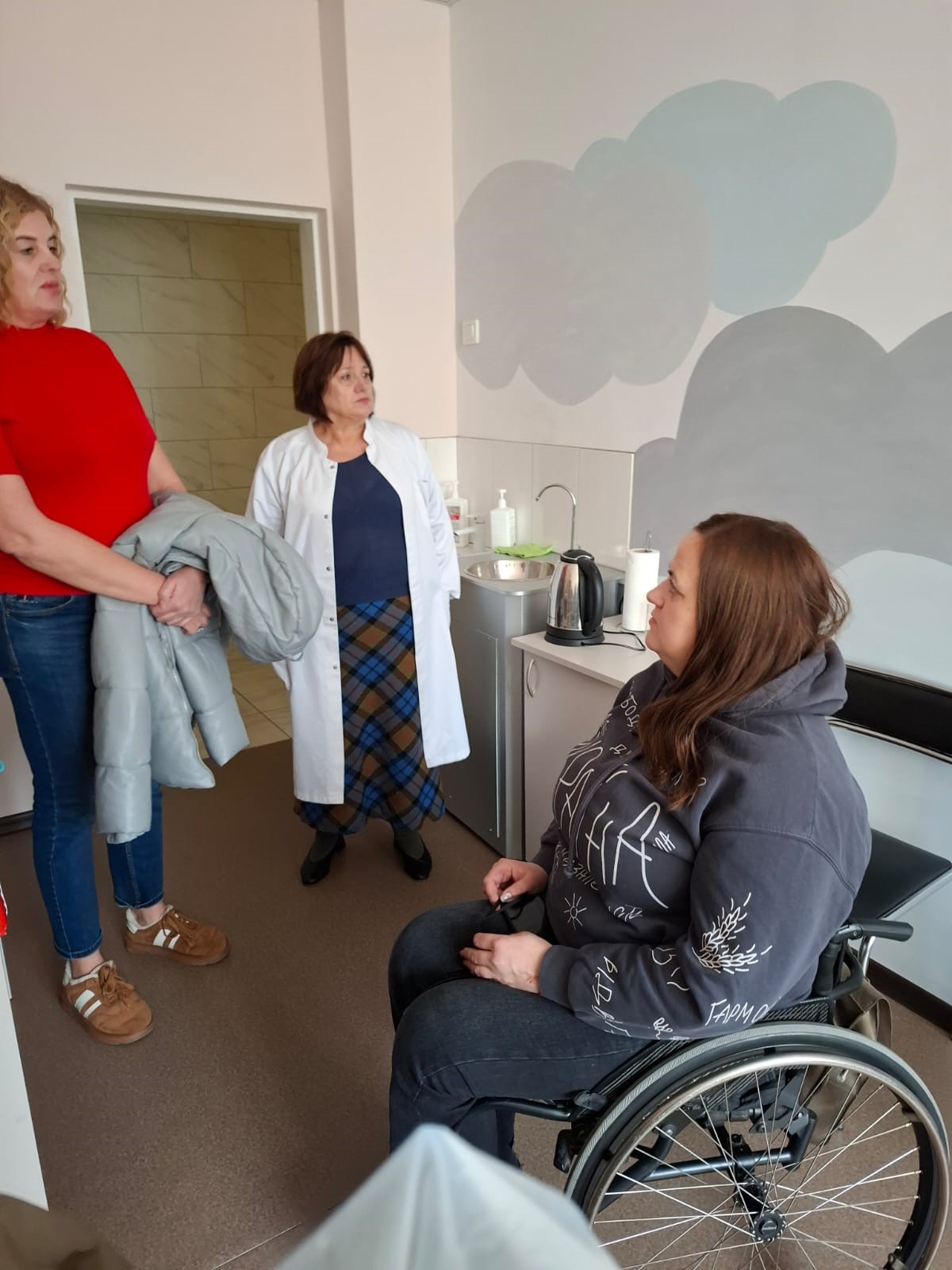 Жінки у кабінеті щось обговорюють. Одна з учасниць розмови у кріслі колісному