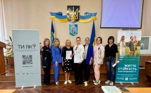 Учасники заходу роблять спільну світлину на фоні банера програми ментального здоров'я "Ти як?"