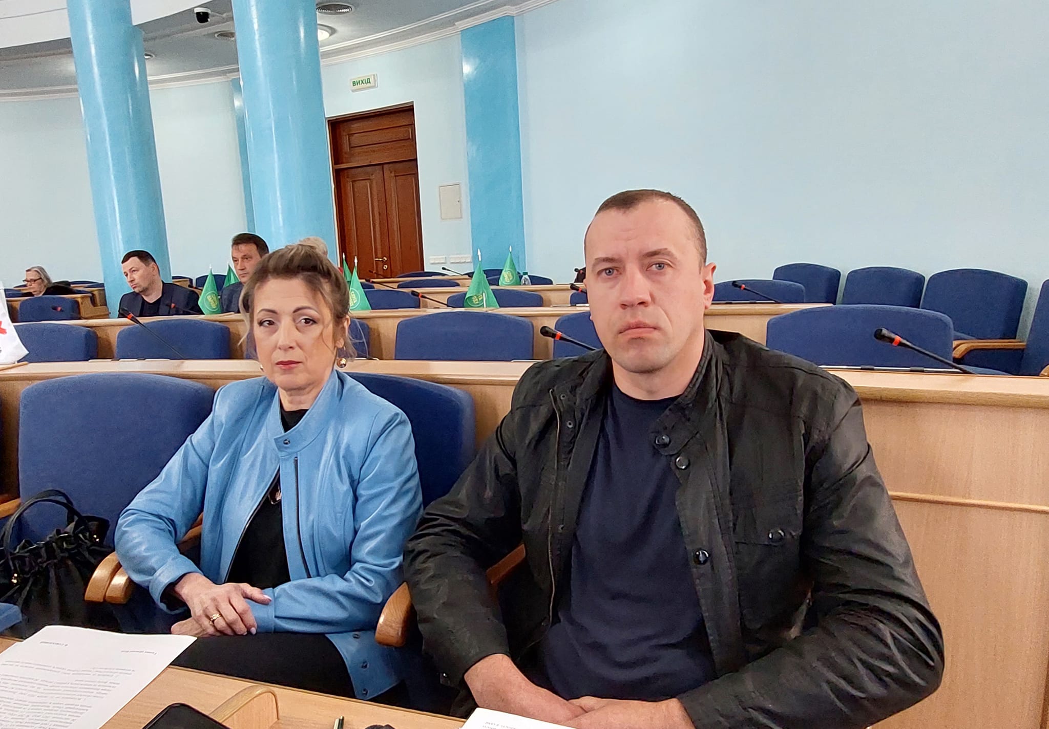 Чоловік та жінка сидять у залі з паперами.