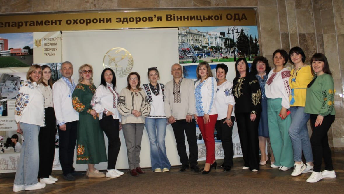 Група людей позує для фото перед плакатом.