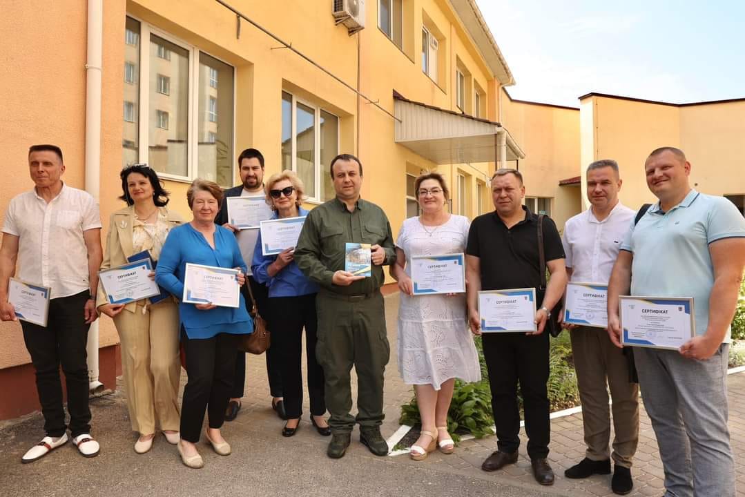 Група людей тримає сертифікати перед будівлею.