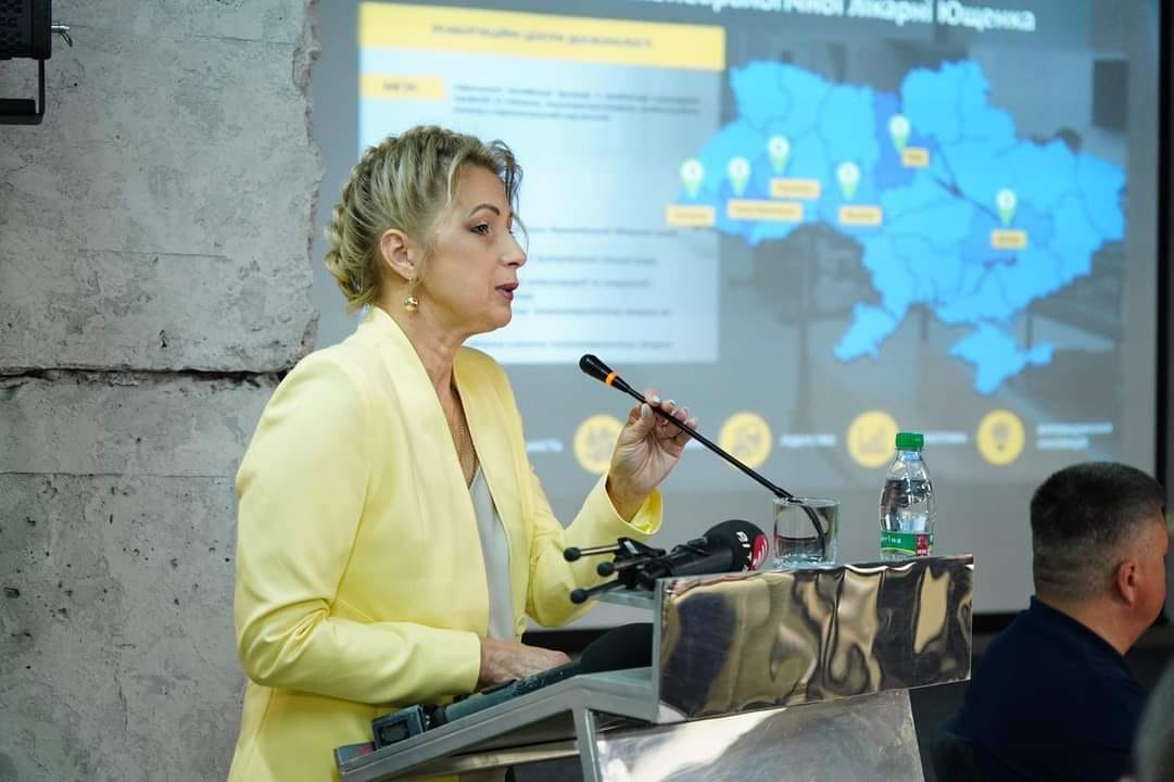 Жінка в жовтій куртці виступає з презентацією.