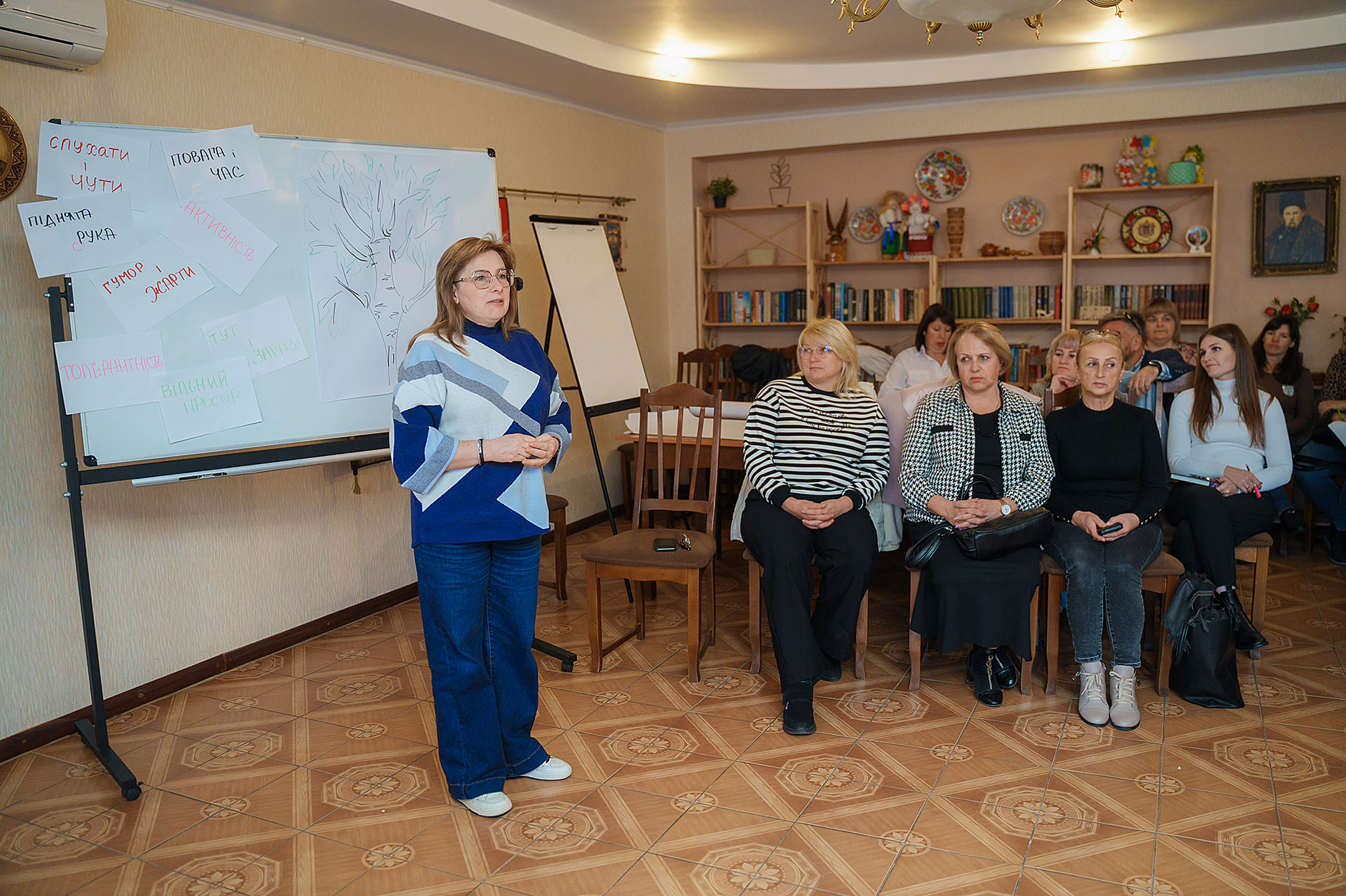 Жінка стоїть перед групою людей, демонструючи впевненість та лідерські якості.