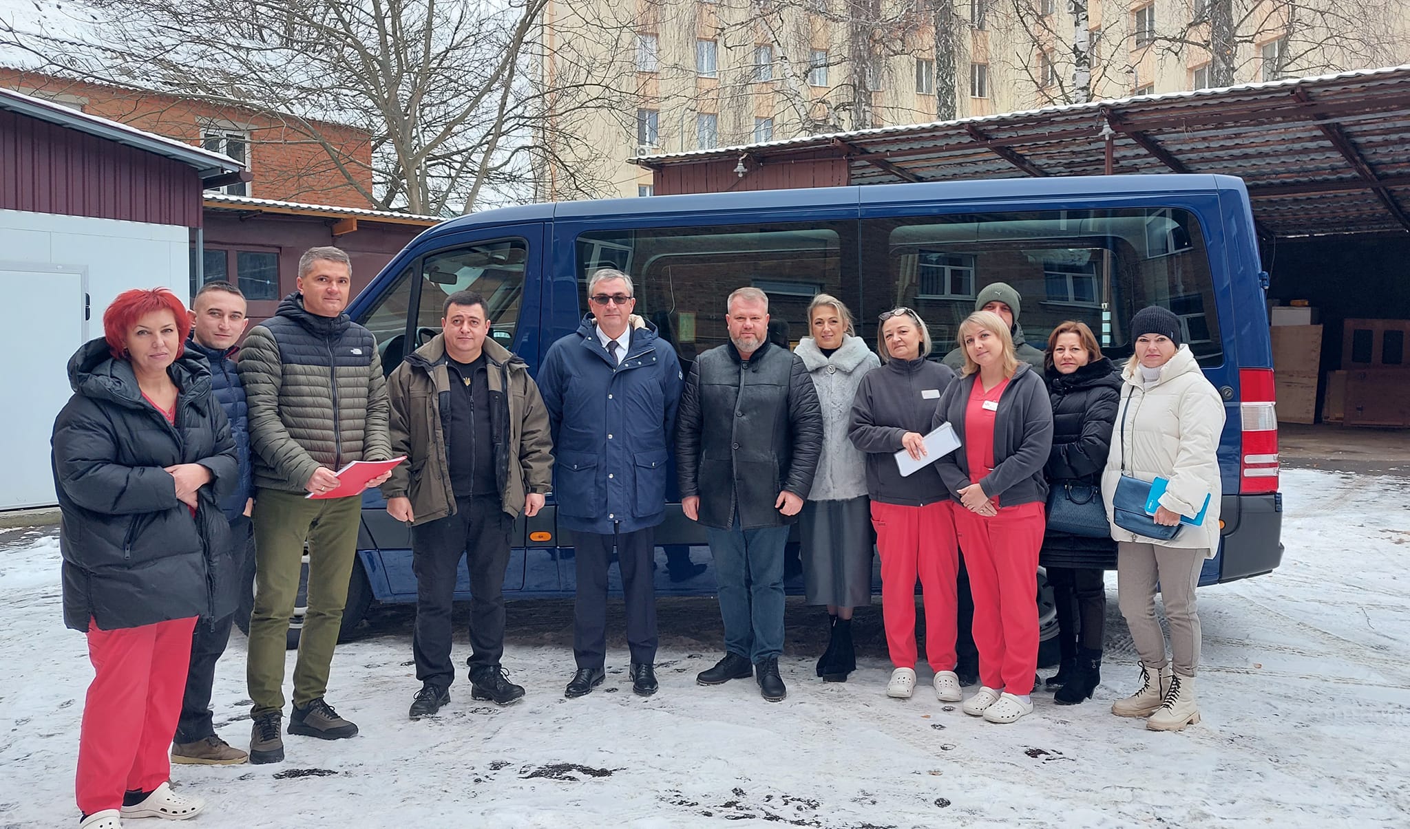 Група людей стоїть перед синім фургоном, усміхаючись та спілкуючись між собою.